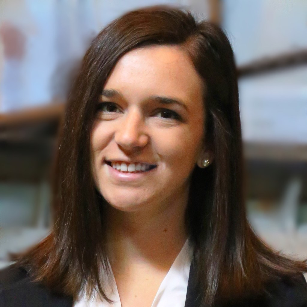 Headshot of a woman smiling at the camera with straight shoulder length brown hair wearing a white shirt and dark jacket.