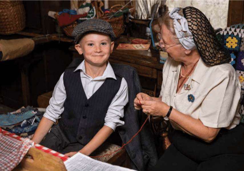 A young person sits next to an older woman who is knitting.